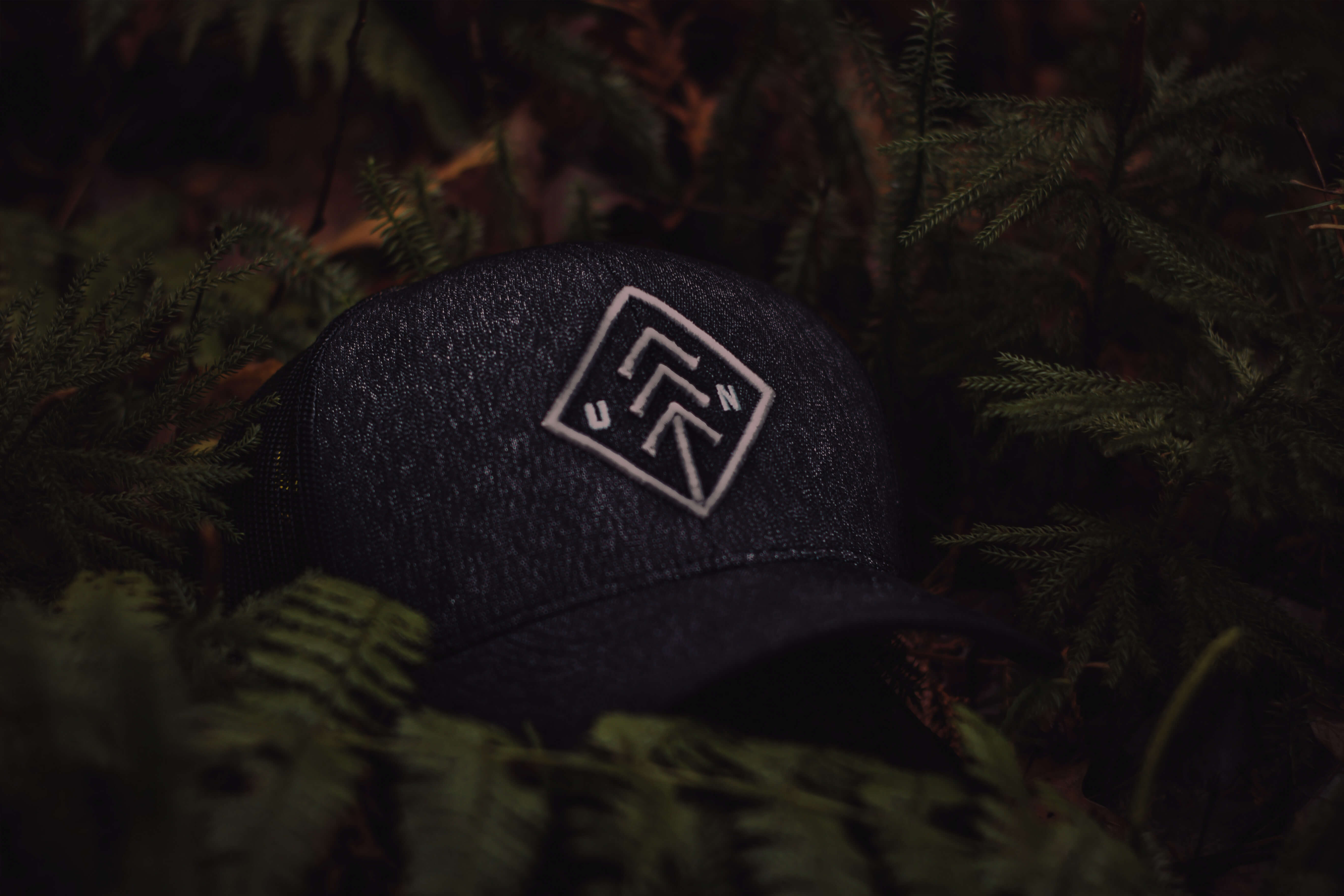 Branded black cloth hat laying in a green bunch of bushes.