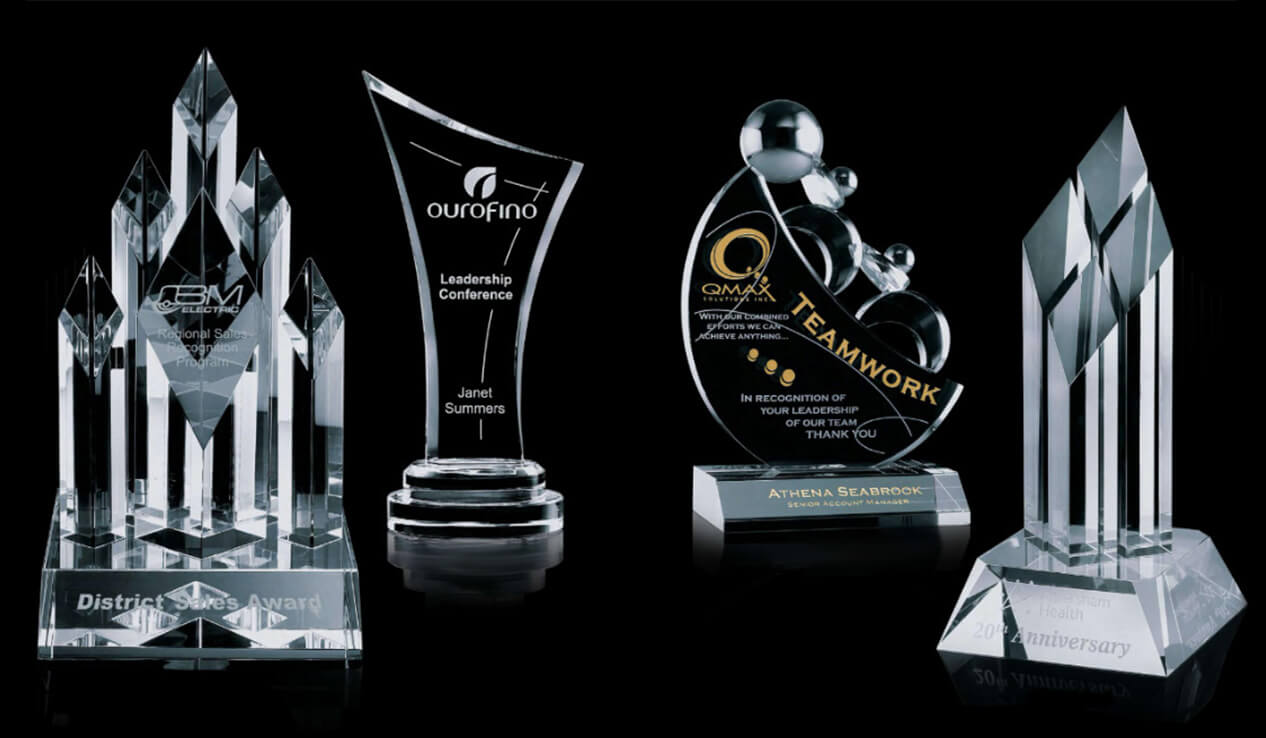 Four glass sandblasts of trophies on a black background.